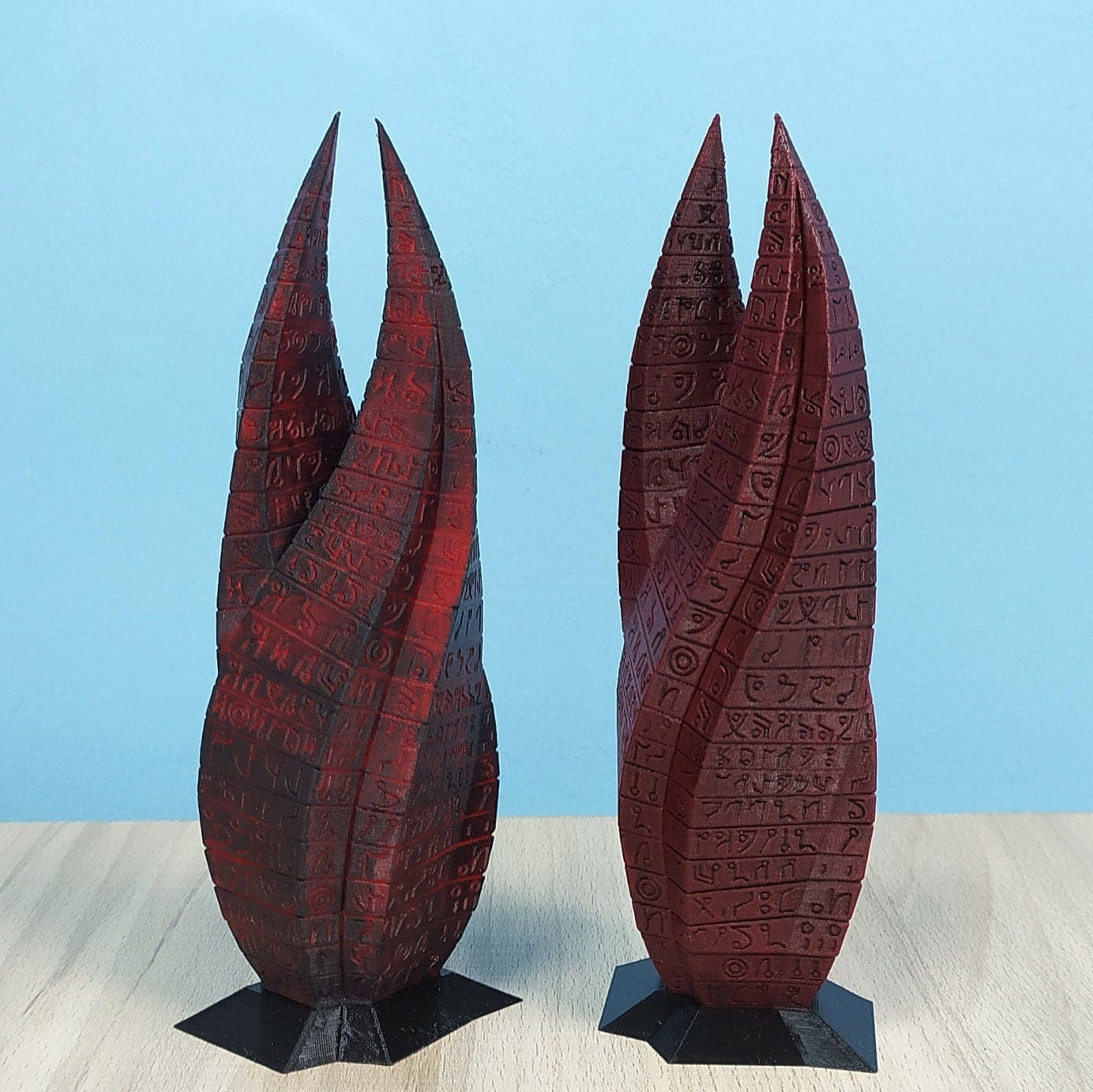 Two red and black textured sculptures on a light gray surface with a blue background