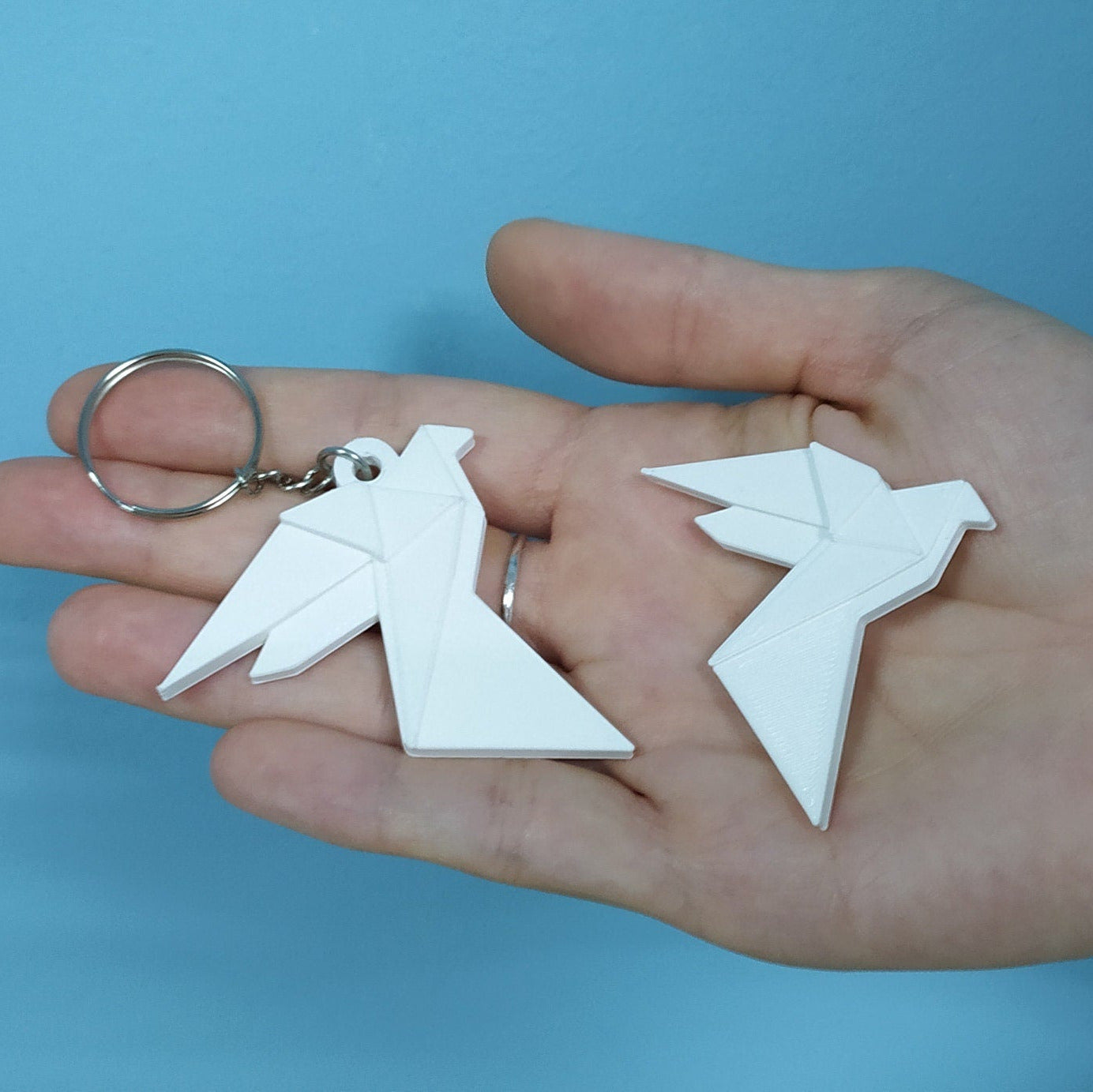 Hand holding two white dove-shaped keychains against a blue background
