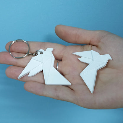 Hand holding two white dove-shaped keychains against a blue background
