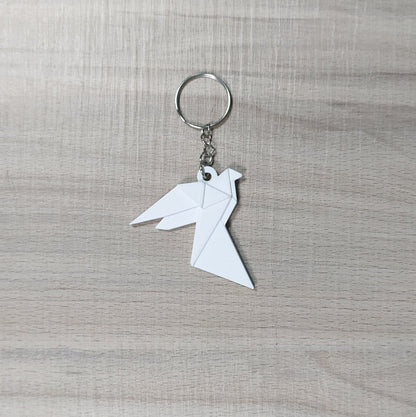 Keychain with a white origami-style bird charm on a gray textured background