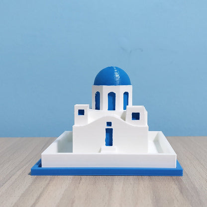 Model of a Greek Orthodox church with a blue dome on a wooden surface and blue background