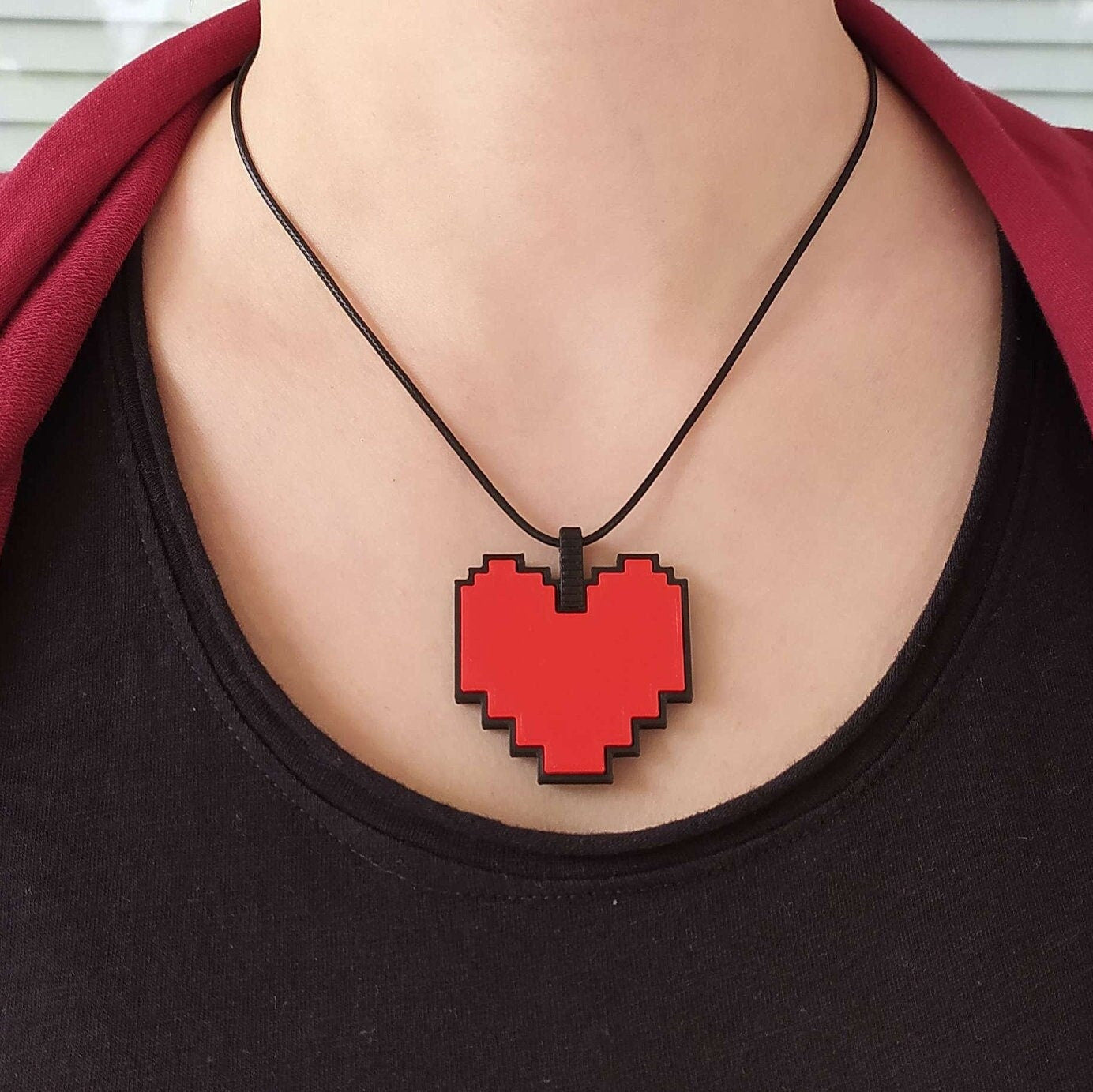 Person wearing a black shirt with a pixelated red heart necklace against a white background from Undertale