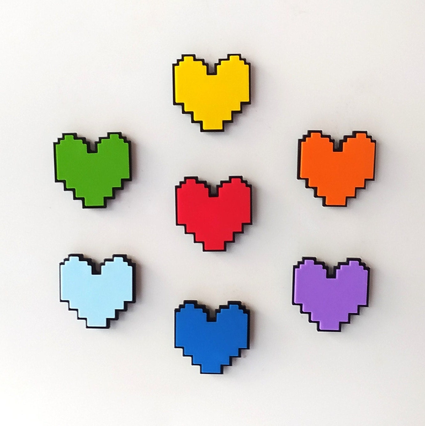 Pixelated heart-shaped pins from Undertale in various colors on a light gray background