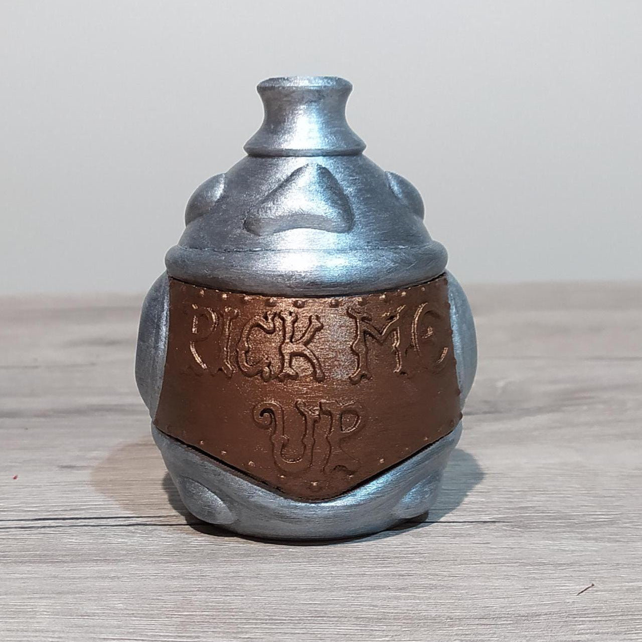 Metallic silver and brown container with 'Pick Me Up' text on a wooden surface