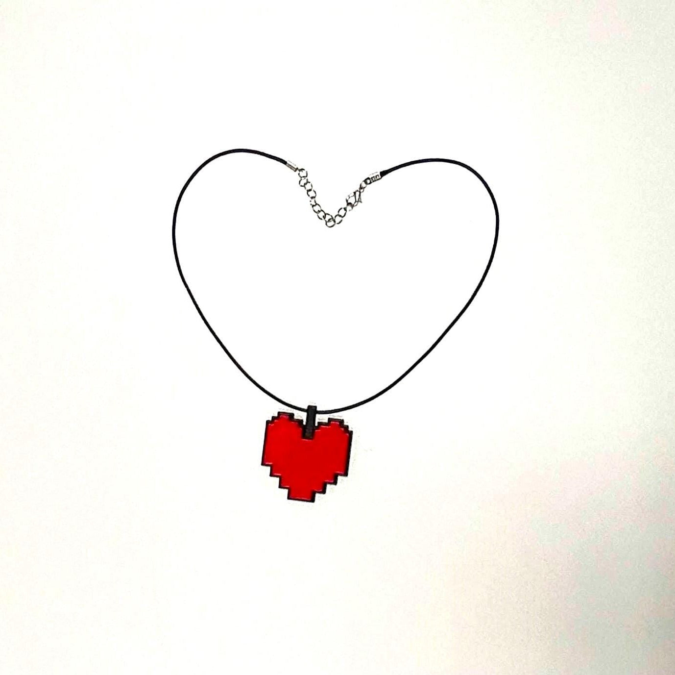 Pixelated red heart from Undertale pendant on a black chain against a white background